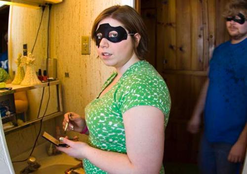 Woman wearing a black caper mask while putting on makeup